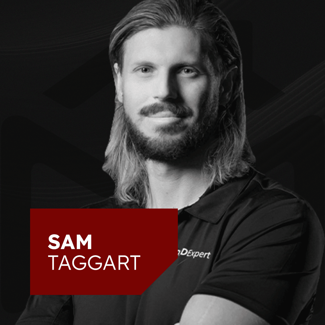 Black and white image of a person with long hair and a beard, wearing a dark shirt. Arms are crossed, and they have a neutral expression. The text "Sam Taggart" is displayed in a bold red rectangle.