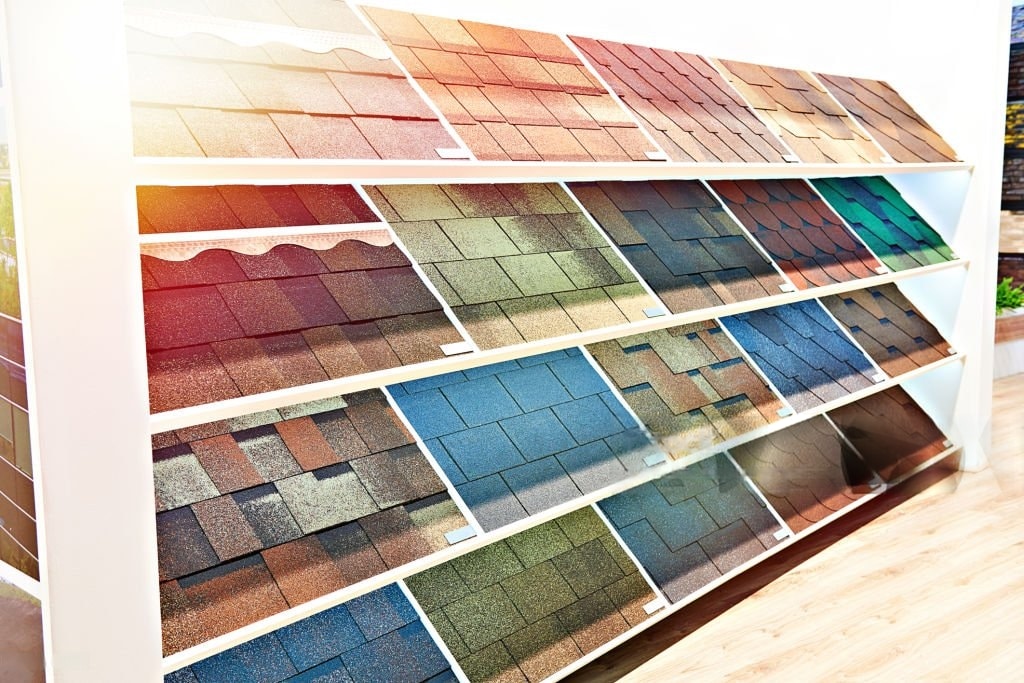Display shelves with various samples of roof shingles in different colors, textures, and patterns, arranged in rows for customer selection in a showroom.